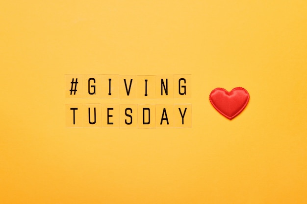 Photo giving tuesday text message. global day of charitable giving after black friday shopping day. red heart on yellow background.