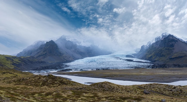 Glacier tongue slides from the Vatnajokull icecap or Vatna Glacier near subglacial Oraefajokull volcano Iceland Glacial lagoon with ice blocks and surrounding mountains