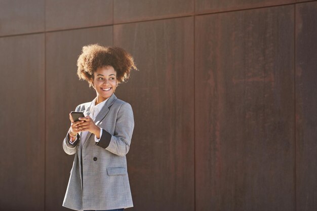 照片高兴的非裔美国妇女使用手机对灰色的墙