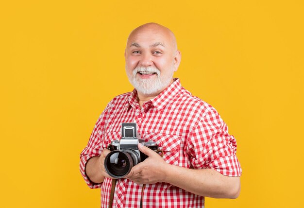 Glad aged man with retro photo camera on yellow baqckground