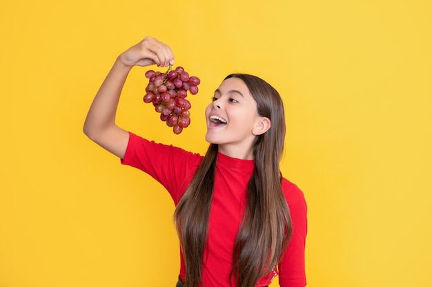 Glad amazed kid hold bunch of grapes on yellow background