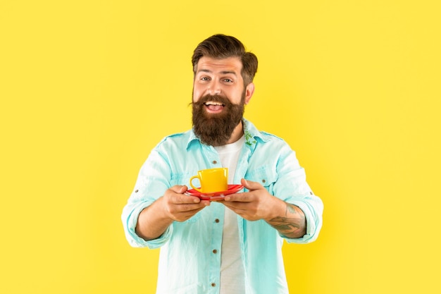 喜んでひげを生やした男は、黄色の背景のバリスタに朝のコーヒーを飲みます