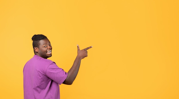 Photo glad black guy pointing finger aside showing copy space studio