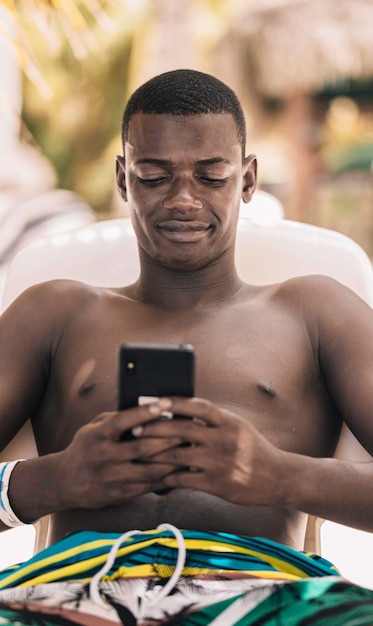 Glad black man using smartphone on beach