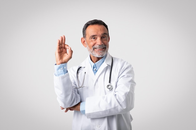 Glad caucasian senior doctor therapist in white coat show ok hand gesture approving health care