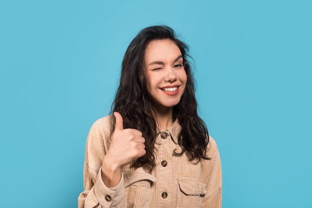 Glad cheerful millennial european woman brunette student in casual showing thumb up winks