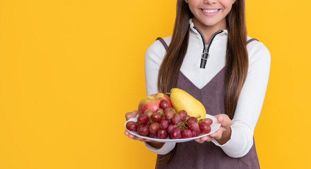 嬉しい子供は黄色の背景にフルーツプレートを保持します