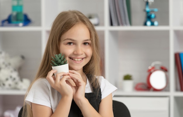 Glad child hold potted plant in school classroom