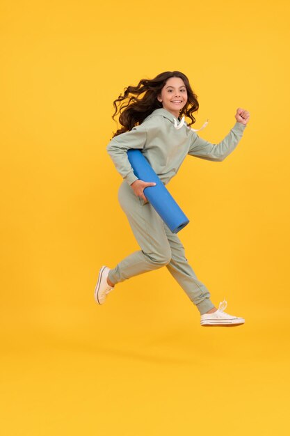 Glad child in sportswear running with fitness mat. fit your body. sport teen girl training.