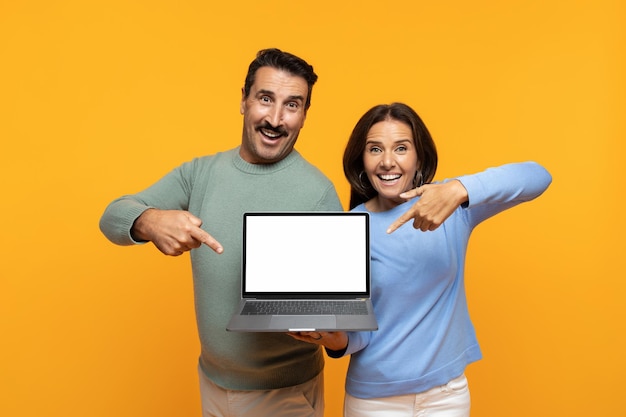 Glad excited funny senior european man and lady point finger at laptop with empty screen