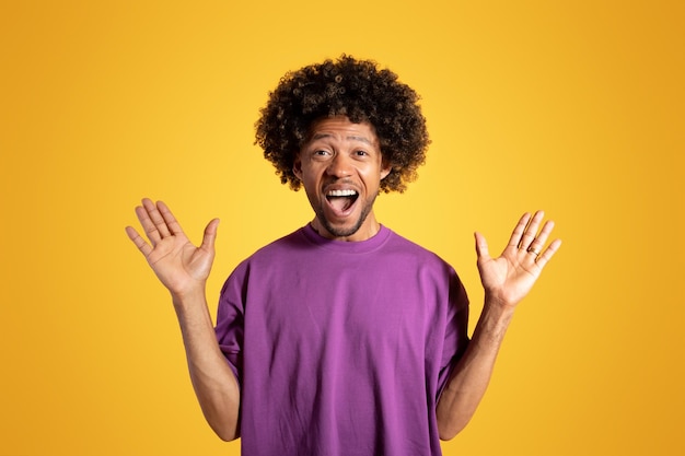 写真 口を開けて手を挙げる紫のtシャツを着た中年のアフリカ系アメリカ人の巻き毛の男が喜んで興奮している