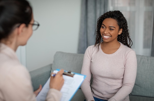 Photo glad happy millennial black lady look at european female doctor in office clinic interior