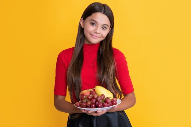 Glad kid hold fresh fruit plate on yellow background