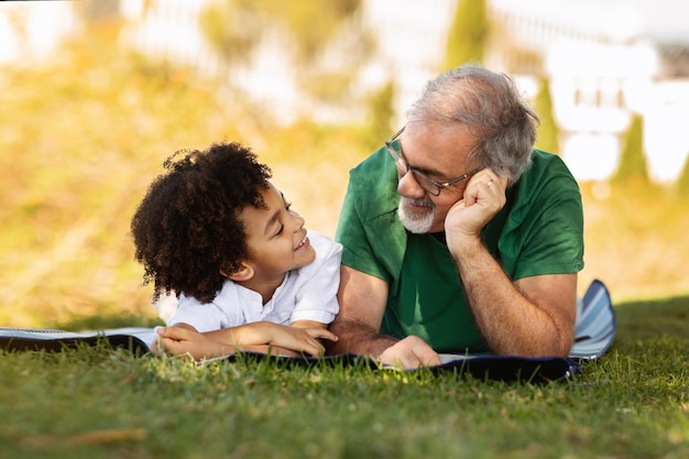 기쁜 작은 혼혈 아이와 노인 백인 할아버지가 녹색 야외에서 자유 시간을 즐깁니다.
