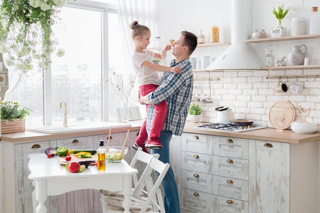 Glad man keeping his daughter in hands at kitchen, copy space