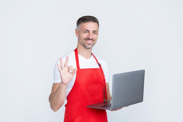 Glad mature man in apron chatting on computer