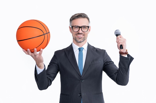 スーツを着てうれしい成熟した男は、白い背景で隔離のバスケットボールボールとマイクを保持します。