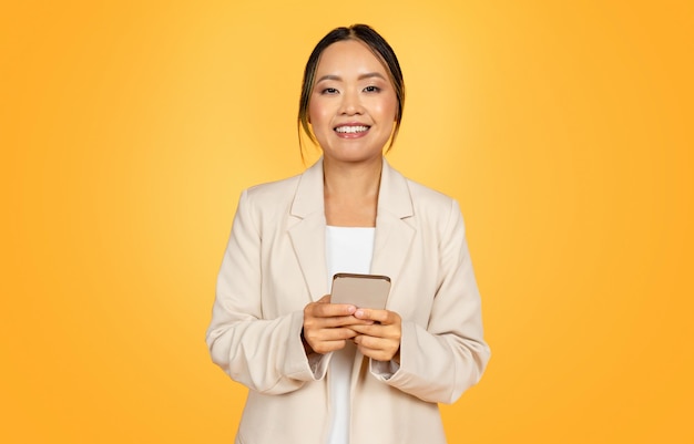 Glad millennial chinese businesswoman in suit typing on smartphone for business