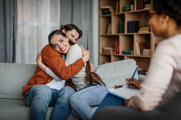 Glad millennial european male and female hugging at meeting with psychologist in office