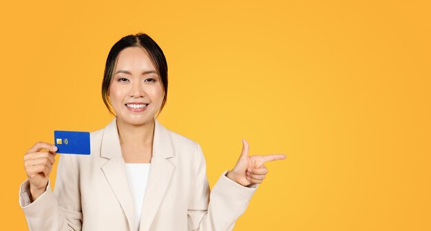 Glad millennial japanese lady in business suit show credit card point finger at copy space