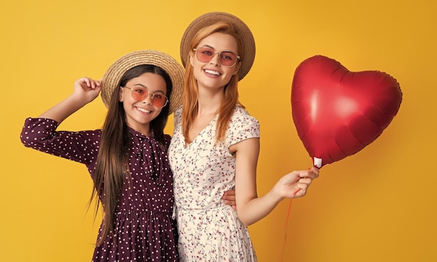 Glad mom and daughter hold love heart balloon on yellow background