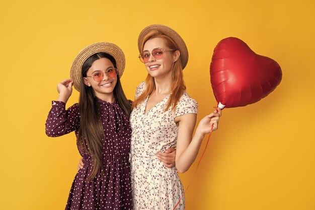 Photo glad mother and daughter hold love heart balloon on yellow background