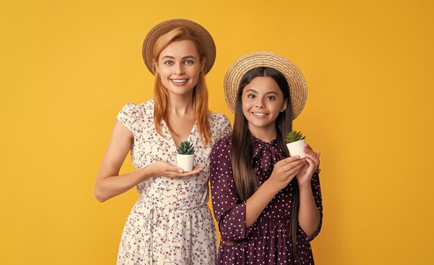 Glad mother and daughter with plant in pot on yellow background