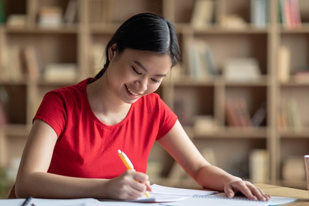 Glad pretty busy smart japanese female make notes at table prepare for exam test in living room