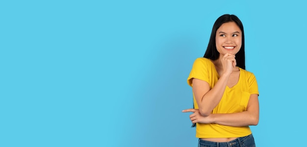 Glad pretty millennial japanese lady student in yellow tshirt looks at empty space and thinks about new order