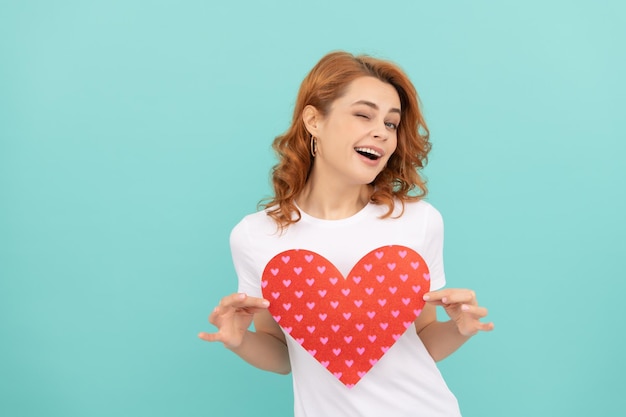 Glad redhead woman hold red heart on blue background