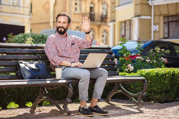 お会いできて嬉しい。ベンチに座っている間彼の友人に挨拶する陽気なハンサムな男