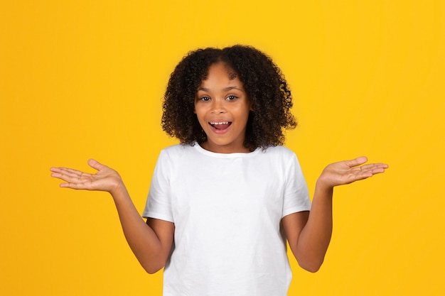 Glad shocked adolescent black girl in white tshirt with open mouth spreads arms to sides holds empty