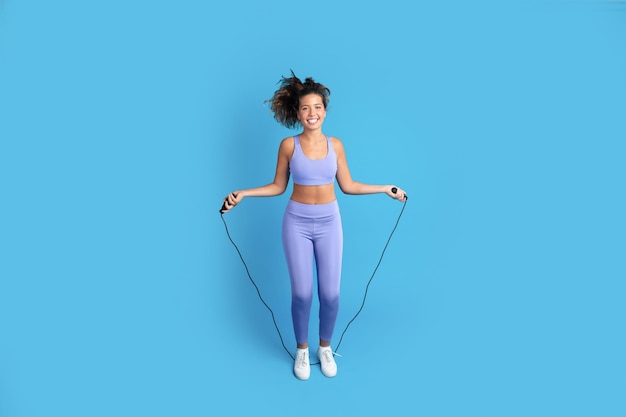 Photo glad slim young caucasian woman in sportswear jumping on jump rope freeze in air