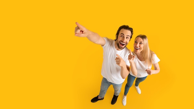 Glad surprised excited millennial caucasian husband and wife in white tshirts pointing up at empty