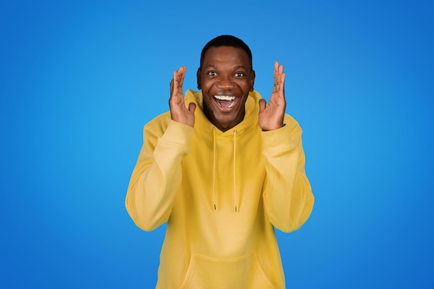 Glad surprised excited young african american guy in sweatshirt gesturing with hands enjoy win