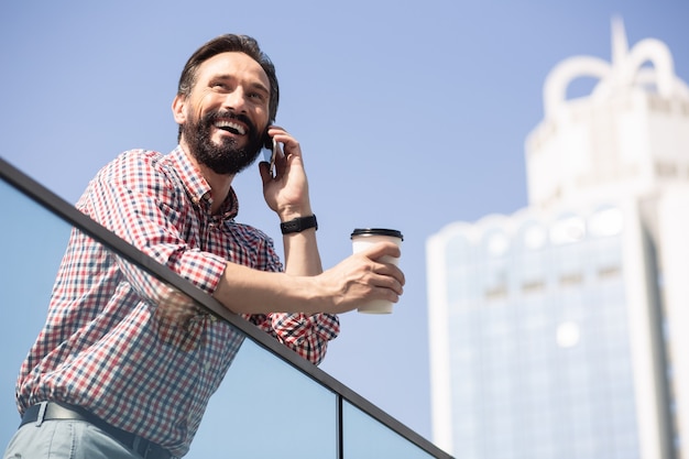 Felice di parlare con te. uomo barbuto allegro che beve caffè e ha una conversazione in città