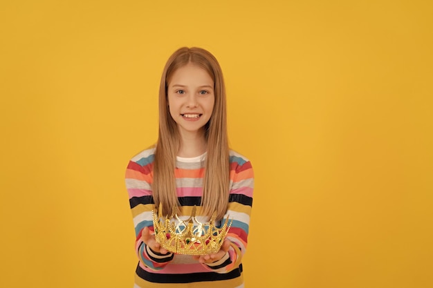 Glad teen child give queen crown on yellow background