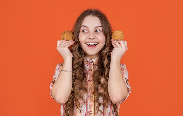Glad teen kid with oatmeal cookies on orange background