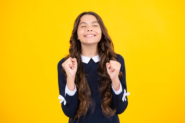 Glad teenager girl crosses fingers closes eyes with pleasure anticipate hearing good news isolated yellow background Happy child rejoices that his dreams came true Excitement concept