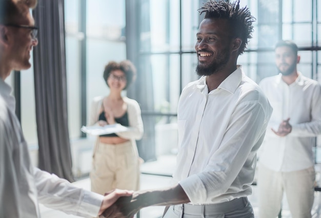 Glad to work with you Young modern men in smart casual wear shaking hands and smiling while working in the creative office