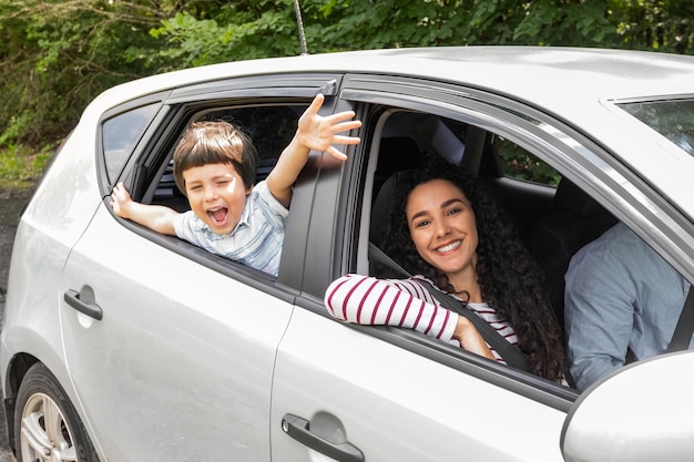 Glad young arabic man and woman driving car little excited boy with open mouth gesturing waving with