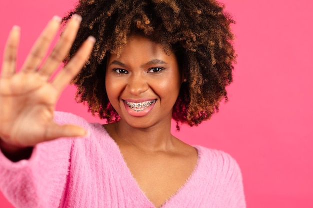 Glad young black curly female in casual with braces waving hand at camera say hello hi making photo