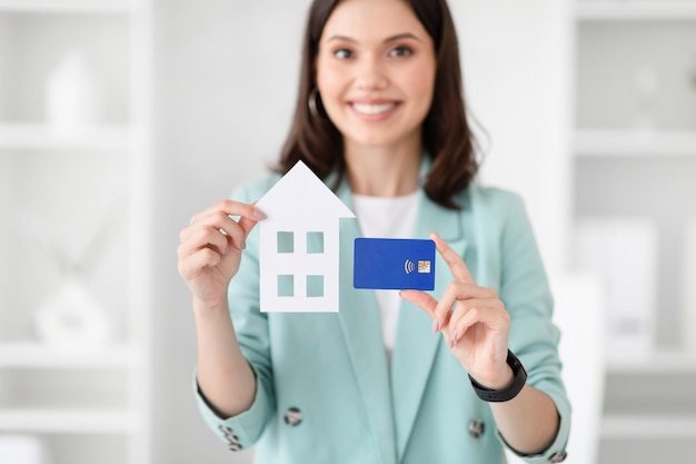 Glad young caucasian businesswoman in suit hold credit card and house