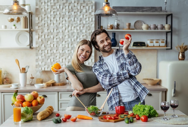 Glad young caucasian guy with stubble and female hold organic vegetables and cooking together