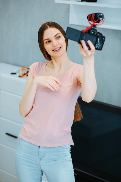 Gladsome jonge dame in vrijetijdskleding die in de woonkamer staat met een camera en microfoon in de hand