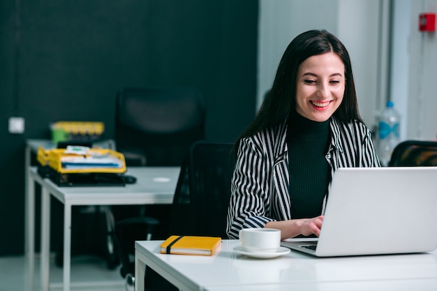 Gladsome young lady in a modern office looking delighted in front of a laptop