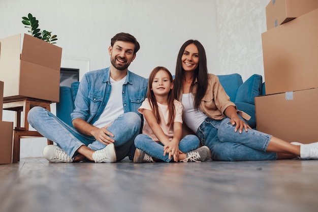 gladsome young man with wife and daughter sitting on a floor between stacks of boxes with packed things