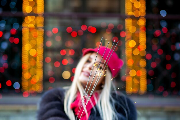 Glamor blonde woman having fun with sparklers against garlands blurred background