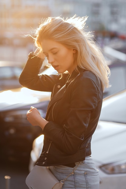 Glamor blonde woman wearing casual jacket and t shirt posing at sunset with sun rays