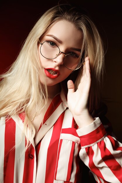 Glamor blonde woman with red lips wearing glasses, posing with colorful light